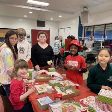 Students gathered around a table completing Christmas crafts.