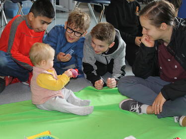 Young students sit and play with the baby visitor