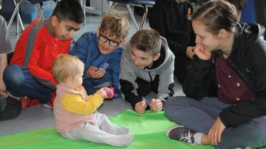 Young students sit and play with the baby visitor